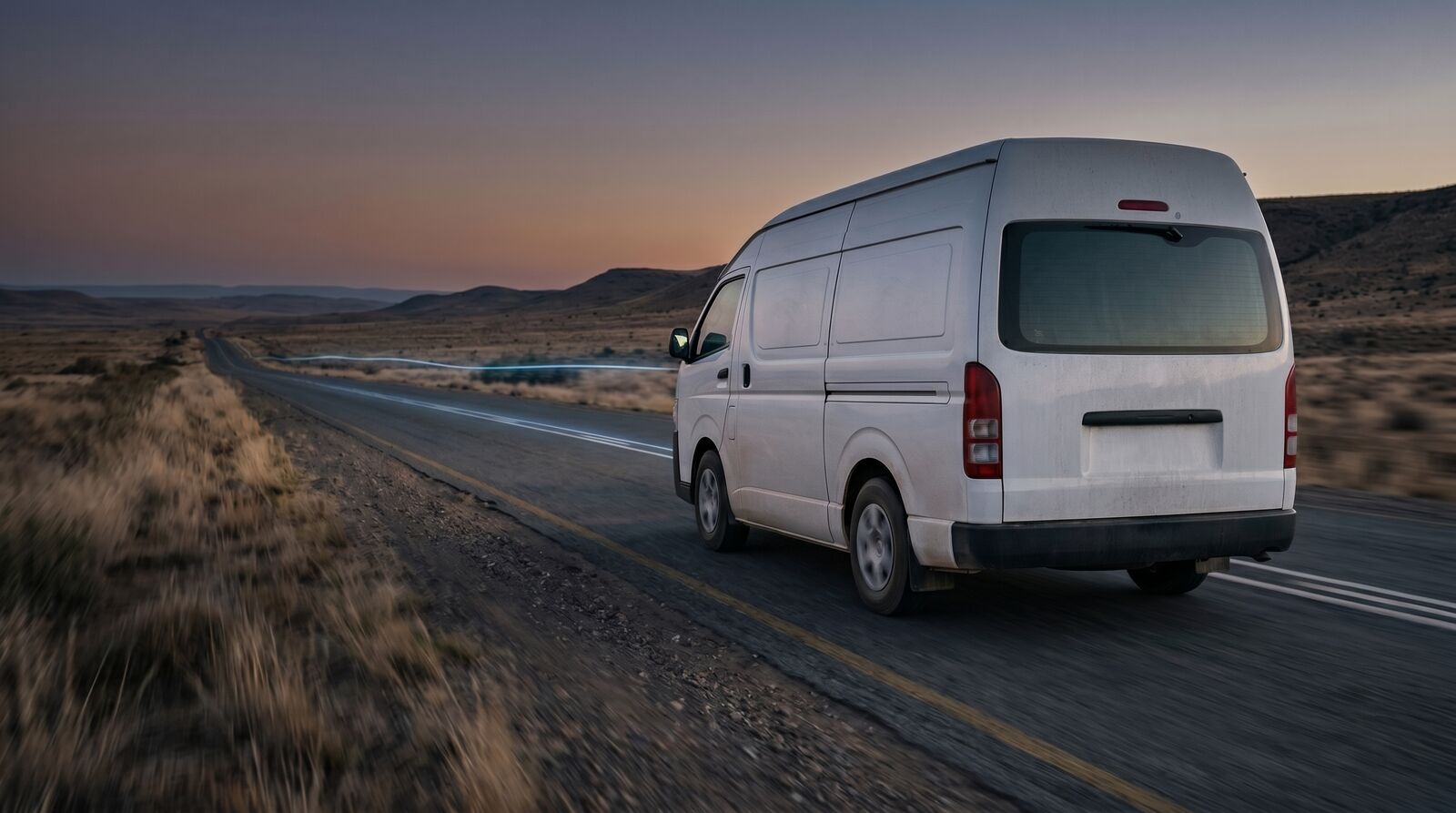 A white commercial van travelling at dusk on an open road through the Karoo
